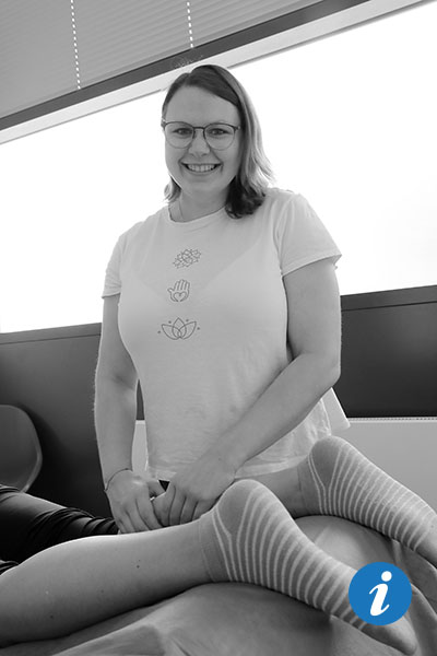 Eine Frau, von der nur die Beine zu sehen sind, liegt auf dem Bauch, eine Physiotherapeutin steht im Hintergrund und lächelt in die Kamera.