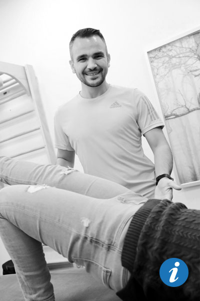 Eine Frau, von der nur Beine und Hüften zu sehen sind, liegt auf dem Rücken, ein Physiotherapeut steht im Hintergrund und lächelt in die Kamera.