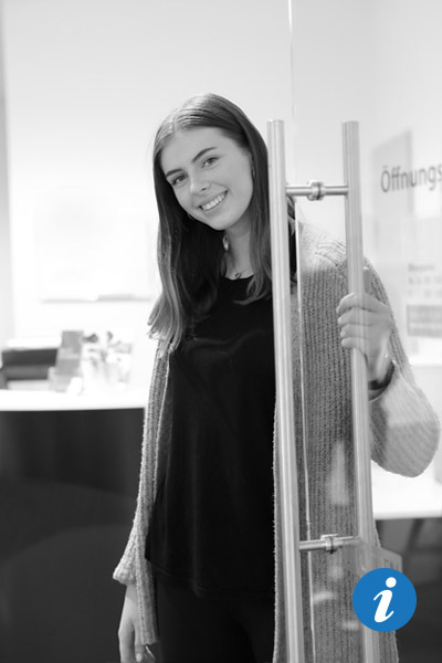 Eine attraktive Frau steht an einer Glastür und hält sie auf.