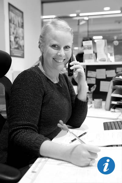 Eine Frau sitzt am Schreibtisch und telefoniert, während sie in die Kamera lächelt.