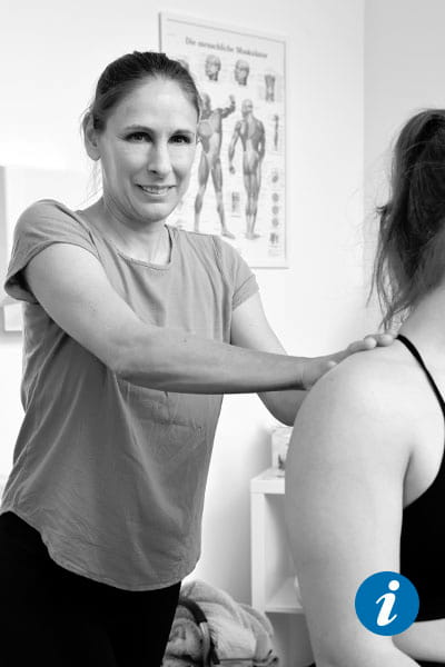 Physiotherapeutin Alex hält ihre Hände auf der Schulter einer Patientin und schaut in die Kamera.